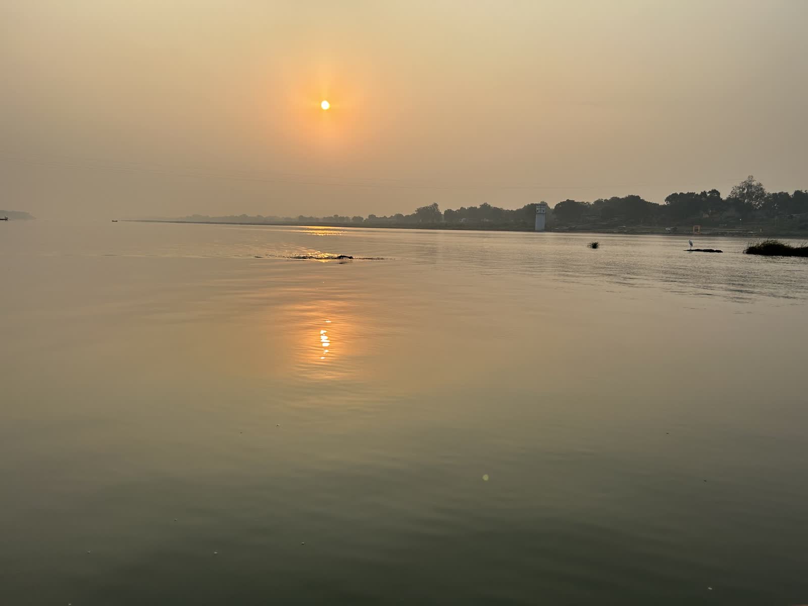 The sun rising over a calm river with a hazy shoreline