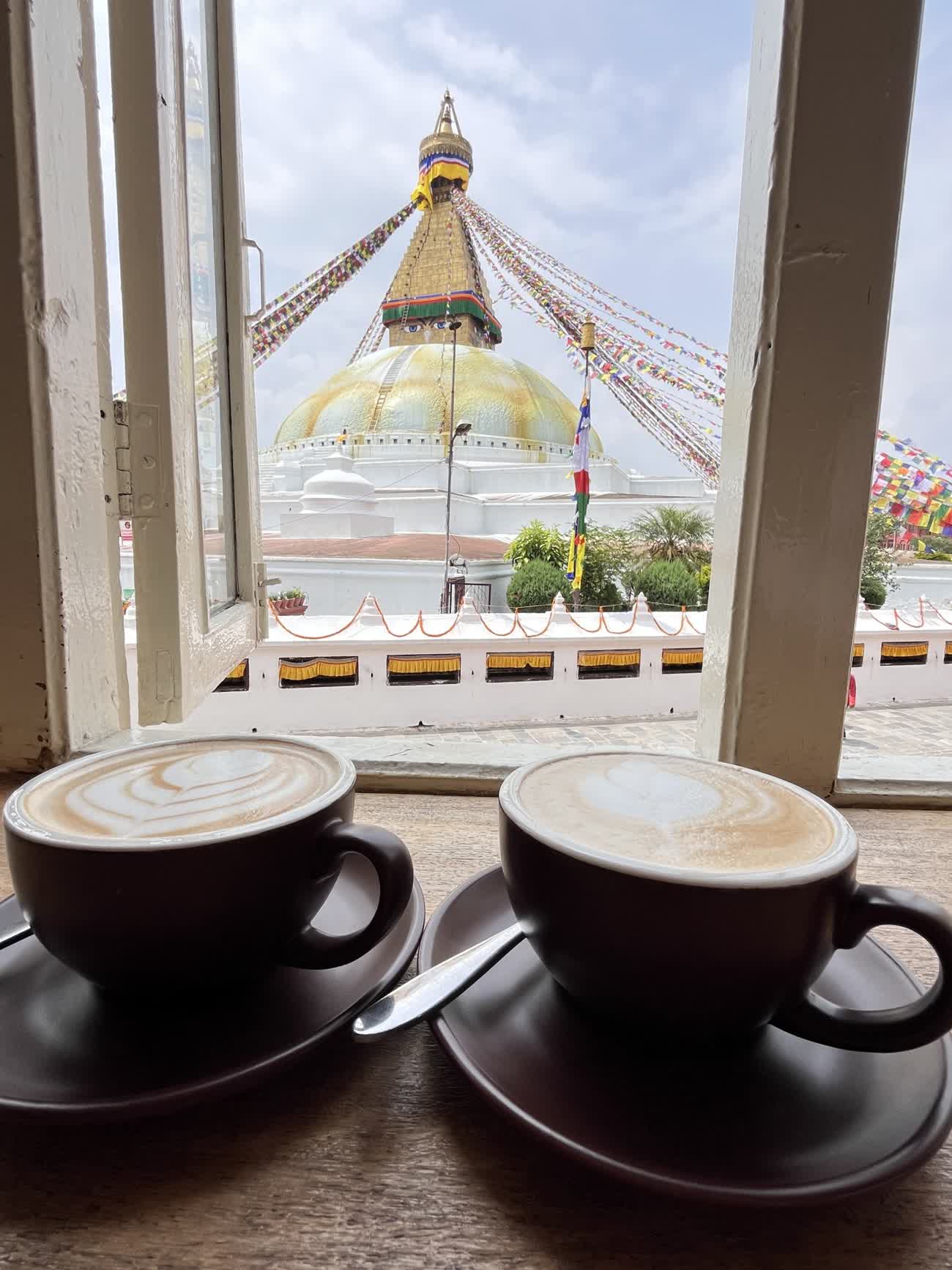 Two cups of latte on a window sill looking out at a golden stupa