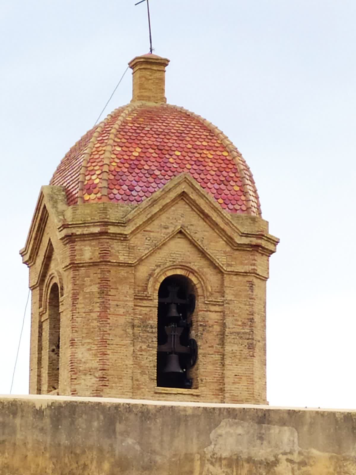 A brick bell tower with a tiled dome and two bells visible in an arched opening