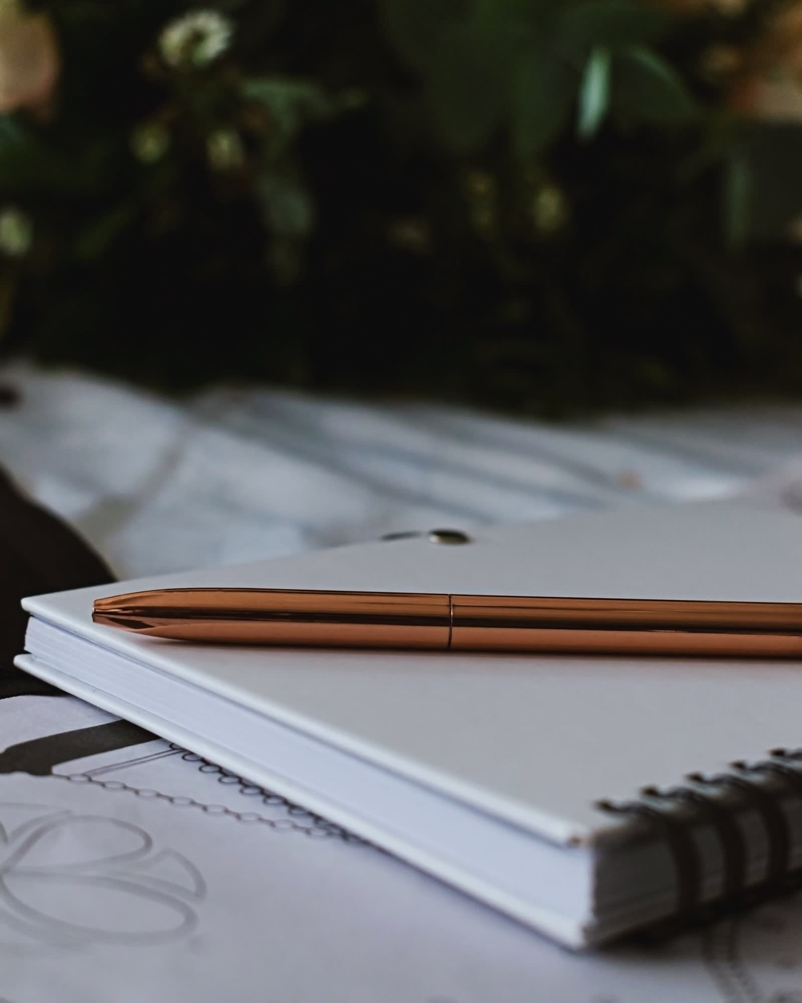 A copper pen resting on a closed spiral-bound notebook