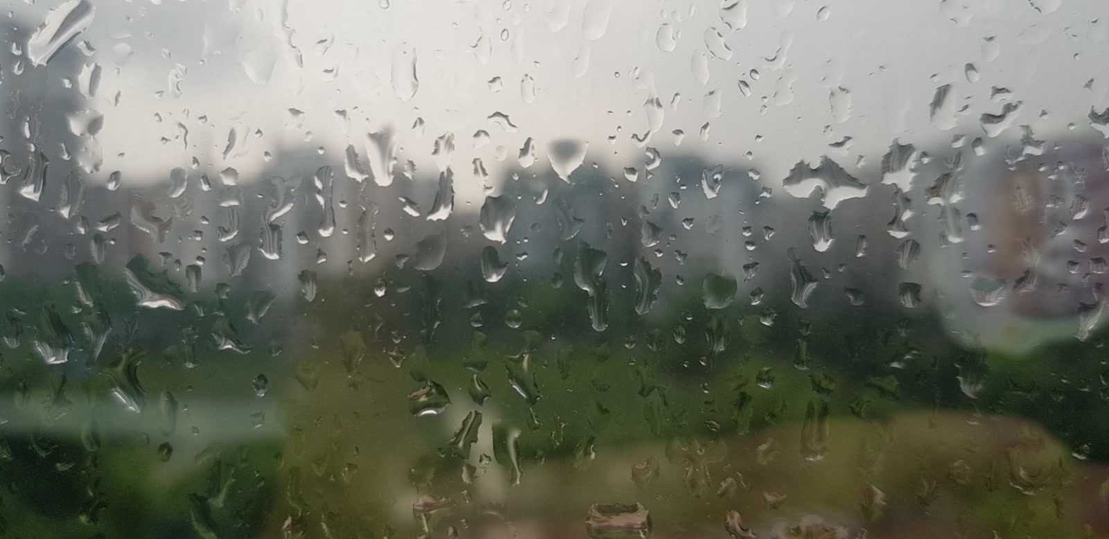 Raindrops on a window pane with a soft grey city view behind