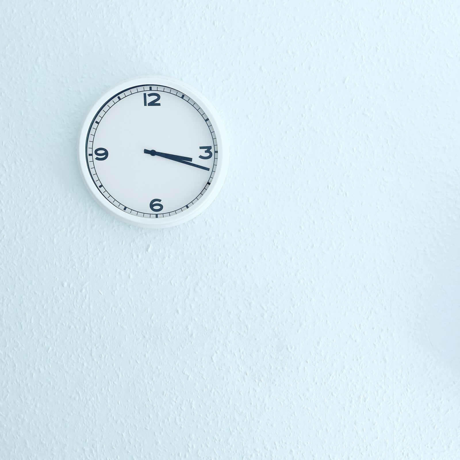A white analog wall clock on a pale blue textured wall