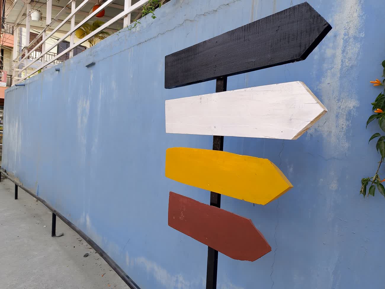 A wooden signpost with four blank colored arrows against a blue wall