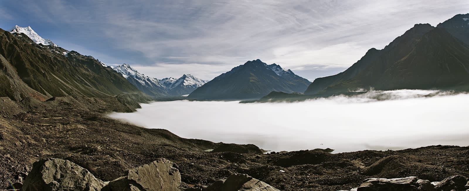 Wide mountain valley with a low bank of white cloud and snow-capped peaks under a blue sky