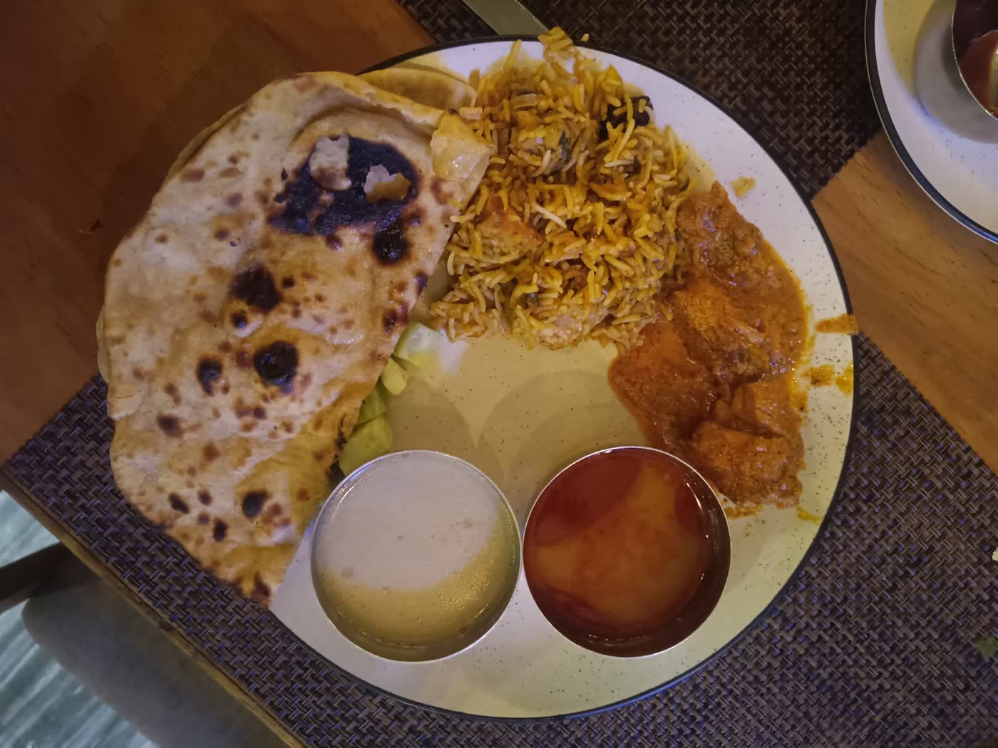 A plate with roti, biryani rice, a curry and two small steel bowls of side dishes