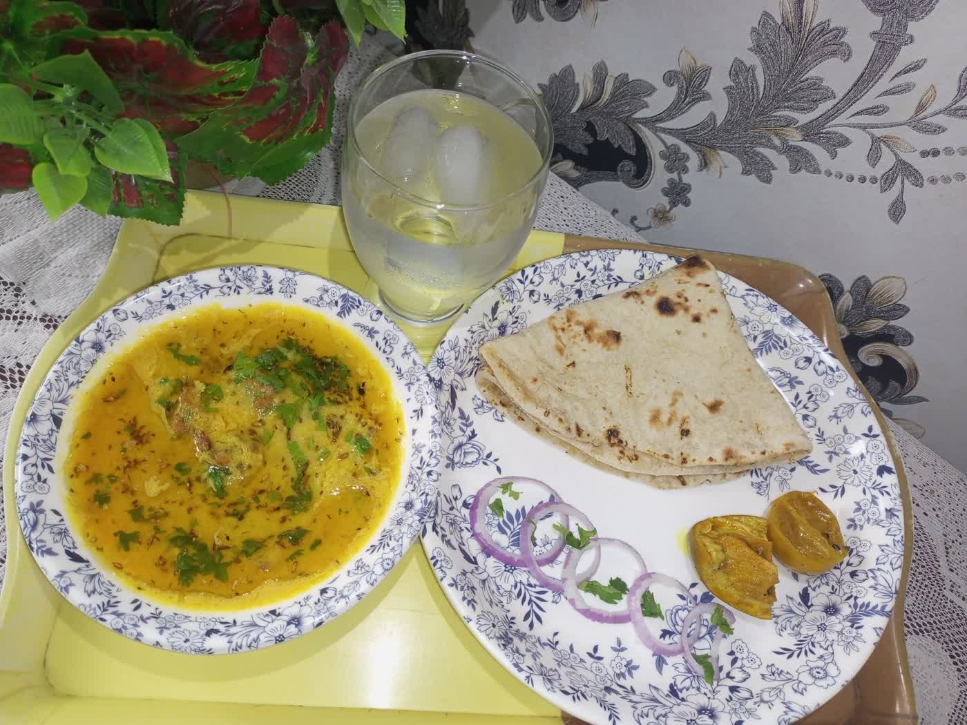 A bowl of yellow dal garnished with cumin and coriander, served beside folded chapati and sliced onion