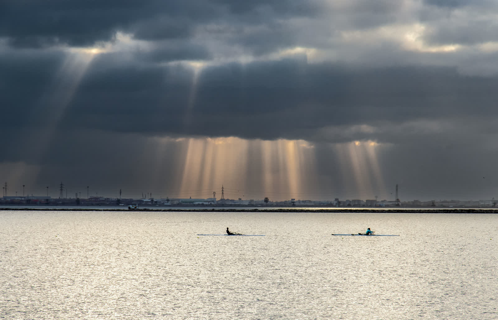 Two small rowing boats on a wide, calm stretch of water beneath dramatic clouds with shafts of light