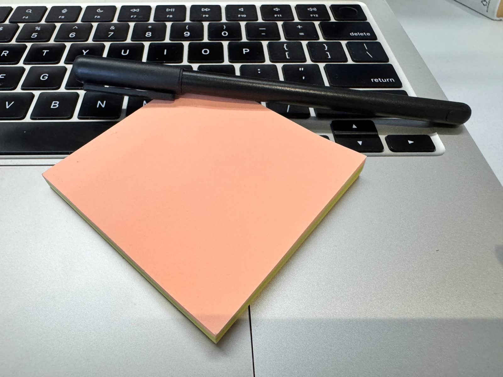 A pad of peach sticky notes and a black pen resting on a laptop keyboard